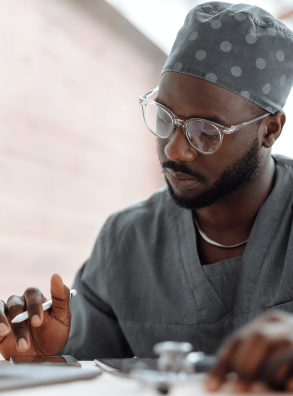 A surgeon looking down at his phone while reviewing papers on the table.